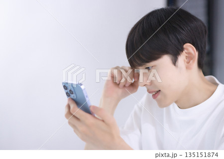 リビングでスマホを見て落胆する若い男性 135151874