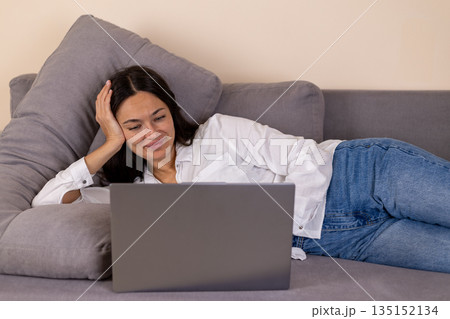 Woman lying on a sofa and working on a laptop. 135152134
