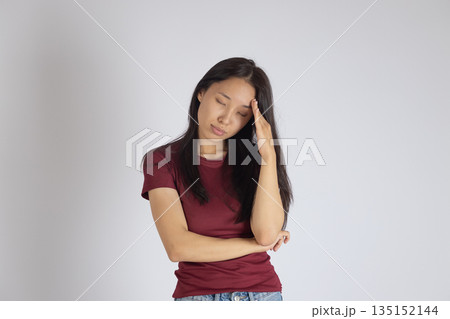 Young woman in burgundy shirt touching her forehead. Young woman in burgundy shirt touching her forehead. 135152144