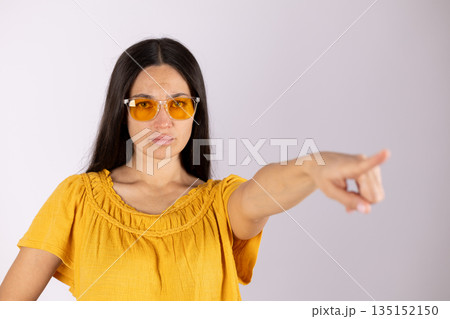 Serious woman in yellow shirt and glasses pointing forward. 135152150