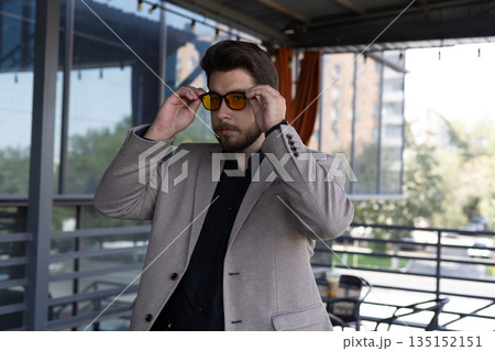 Man in a jacket adjusting his sunglasses outdoors. Man in a jacket adjusting his sunglasses outdoors. 135152151