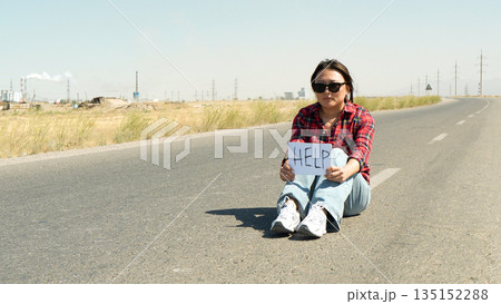 Woman traveler sitting on the side of a road. 135152288