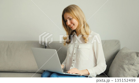 Happy modern woman working with laptop, freelancer girl sitting on a couch in the living room 135152499