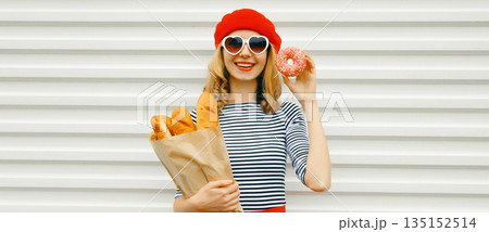Happy cheerful smiling young woman holding grocery shopping paper bag with white bread baguette 135152514