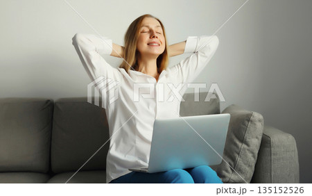 Happy young woman relaxes while working on laptop, freelancer girl enjoys free time sitting at home 135152526