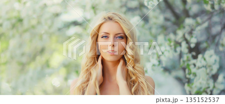 Beautiful blonde young woman in spring blooming garden on a sunny day against flowers trees Beautiful blonde young woman in spring blooming garden on a sunny day against flowers trees 135152537