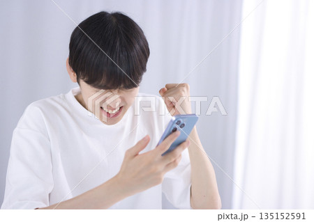 リビングでスマホを見てガッツポーズをする若い男性 リビングでスマホを見てガッツポーズをする若い男性 135152591