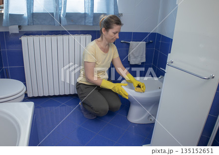 Woman in yellow rubber gloves scrubbing a bidet with a sponge, cleaning bathroom surfaces for hygiene and home maintenance as part of everyday household chores and care 135152651