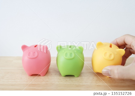 カラフルな3つの豚の貯金箱が並ぶ、貯蓄イメージ。 カラフルな3つの豚の貯金箱が並ぶ、貯蓄イメージ。 135152726