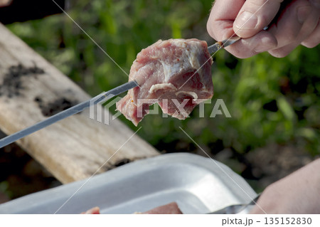 A man prepares food. Hand threads a piece of raw pork with onions onto a skewer. Close-up. 135152830