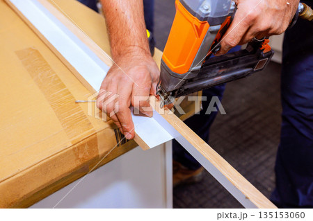 Contractor uses air nail gun to attach pieces of wood together on workbench 135153060