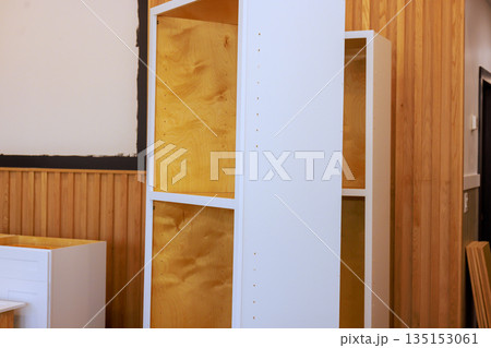 Shelving unit made of wood is placed in room with wood panels part of wall that is still unfinished. 135153061