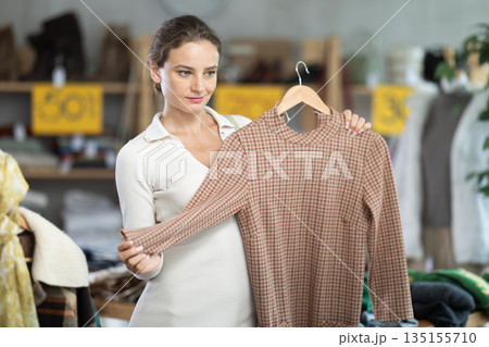 Young woman chooses warm dress in clothing store Young woman chooses warm dress in clothing store 135155710