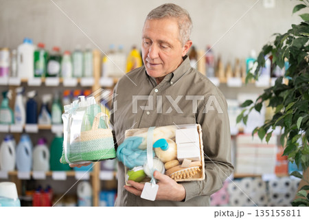 Senior man studies label and choose shower cosmetic present, packaged in basket. 135155811