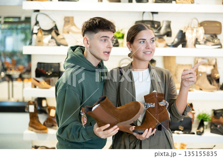 Interested guy helping girlfriend choose demi-season shoes at footwear retailer Interested guy helping girlfriend choose demi-season shoes at footwear retailer 135155835