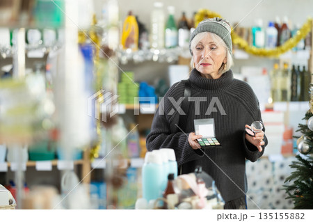 Elderly woman chooses cosmetics and eye shadow in supermarket before Christmas Elderly woman chooses cosmetics and eye shadow in supermarket before Christmas 135155882