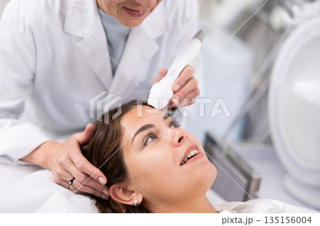 Young woman having face laser therapy procedure by specialist 135156004