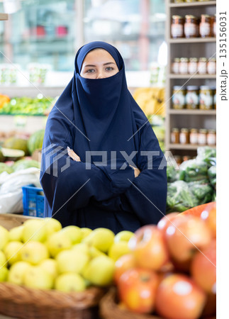 Young muslim female shopper in niqab standing in grocery store Young muslim female shopper in niqab standing in grocery store 135156031