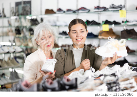 Young colleague shows elderly lady advantages of thick sole in modern sneakers 135156060