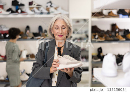Senior woman takes samples from showcase and examines snickers 135156084
