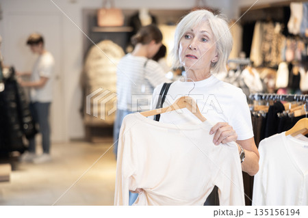 elderly lady carefully examines selection of sweaters 135156194