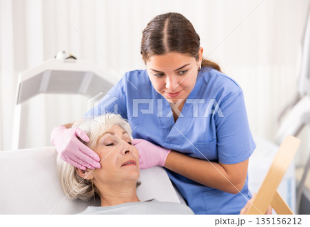Old woman having consultation about face aesthetic while looking in the mirror 135156212