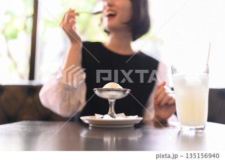 カフェでアイスクリームを食べる笑顔の若い女性 カフェでアイスクリームを食べる笑顔の若い女性 135156940