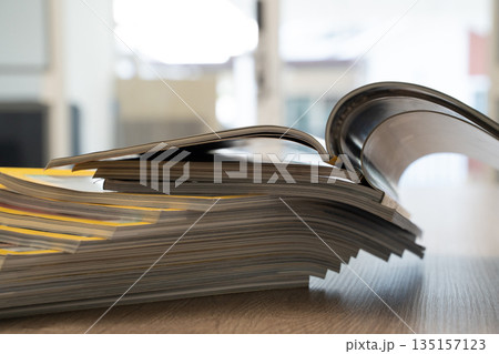 Close up of stacked open magazines showing curved pages and blurred background. Publishing, journalism and printed media concept with room for text. Close up of stacked open magazines showing curved pages and blurred background. Publishing, journalism and printed media concept with room for text. 135157123