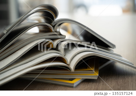 Close up of stacked open magazines showing curved pages and blurred background. Publishing, journalism and printed media concept with room for text. 135157124
