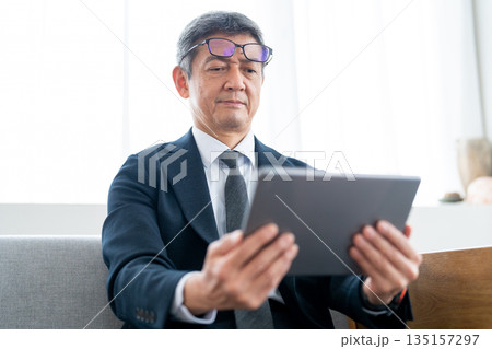 老眼鏡を頭に乗せてタブレット端末を操作するシニア男性 135157297