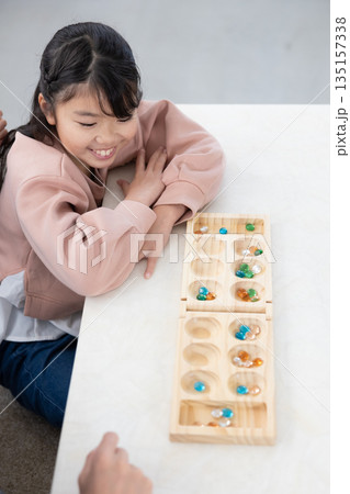 自宅のリビングでマンカラを楽しむ小学生の女の子 自宅のリビングでマンカラを楽しむ小学生の女の子 135157338