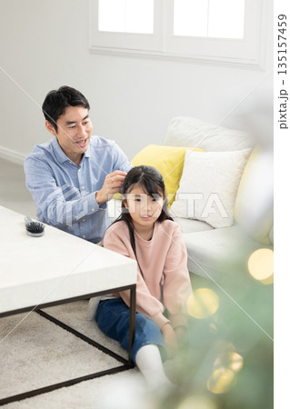 リビングで娘の髪を結ぶ父親 リビングで娘の髪を結ぶ父親 135157459