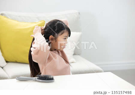 リビングルームで髪を縛る小学生の女の子 135157498