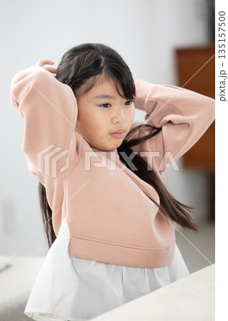 リビングルームで髪を縛る小学生の女の子 リビングルームで髪を縛る小学生の女の子 135157500