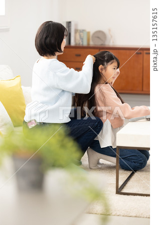 自宅のリビングで母親に髪をセットしてもらう小学生の女の子 自宅のリビングで母親に髪をセットしてもらう小学生の女の子 135157615