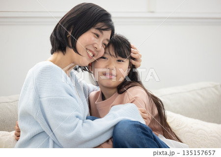 リビングのソファでふれあう母親と小学生の女の子 135157657