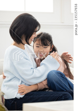 リビングのソファでふれあう母親と小学生の女の子 135157658
