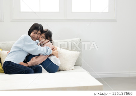 リビングのソファでふれあう母親と小学生の女の子 リビングのソファでふれあう母親と小学生の女の子 135157666