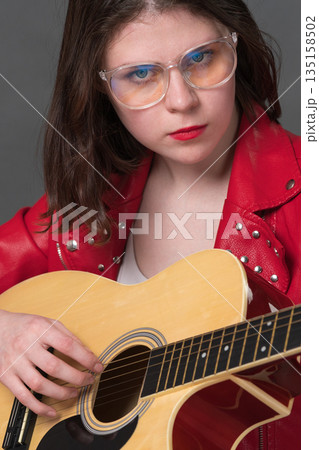 Close-up view of female guitarist strumming strings her acoustic musical instrument and looking at camera 135158502