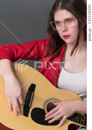 Portrait of female guitarist, she holding her musical instrument in front of her, with guitar resting on lap. She looking intently into distance, suggesting state of deep contemplation, concentration 135158505