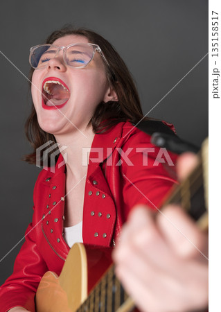 Woman in euphoria plays guitar and sings song with great fervor. Rock musician in state of pure bliss, with her eyes closed, mouth wide open, and voice resonating with a powerful emotional intensity Woman in euphoria plays guitar and sings song with great fervor. Rock musician in state of pure bliss, with her eyes closed, mouth wide open, and voice resonating with a powerful emotional intensity 135158517