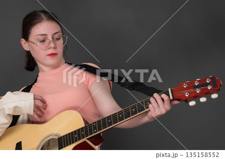 Confident female guitarist concentrating on strumming acoustic guitar and looking down at guitar neck while learning to play an instrument. Authentic musician wearing eyeglasses, dressed in pink shirt Confident female guitarist concentrating on strumming acoustic guitar and looking down at guitar neck while learning to play an instrument. Authentic musician wearing eyeglasses, dressed in pink shirt 135158552