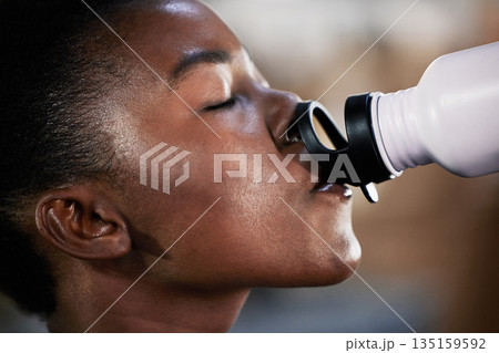 Face, fitness or black woman drinking water in gym after training, workout or exercise to relax or hydrate body. Tired, fitness or tired girl with bottle for healthy liquid hydration on resting break Face, fitness or black woman drinking water in gym after training, workout or exercise to relax or hydrate body. Tired, fitness or tired girl with bottle for healthy liquid hydration on resting break 135159592