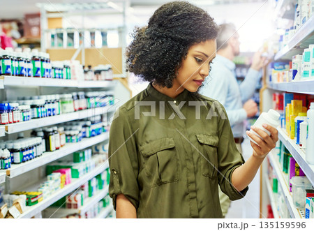 Pharmacy, health shop and woman with medicine for reading label, check product and choice in retail store. African female person looking at drugstore pills for ingredients, information and shopping 135159596