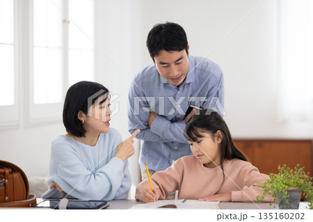 自宅で子供に勉強を教えながら困った表情をする両親 自宅で子供に勉強を教えながら困った表情をする両親 135160202