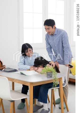 自宅で勉強中にテーブルに顔を伏せる小学生と困った表情の両親 自宅で勉強中にテーブルに顔を伏せる小学生と困った表情の両親 135160216