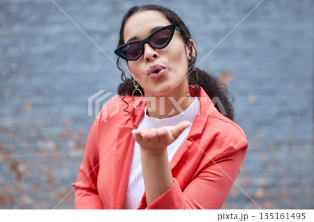 Fashion, blowing kiss and portrait of woman on wall background in trendy, stylish and cool clothes. Beauty, flirt and happy female person pose in city with sunglasses, confidence and style outdoors Fashion, blowing kiss and portrait of woman on wall background in trendy, stylish and cool clothes. Beauty, flirt and happy female person pose in city with sunglasses, confidence and style outdoors 135161495