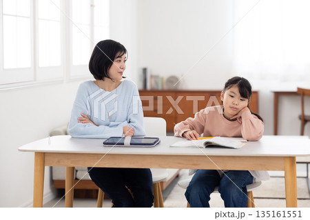 自宅で勉強する小学生の女の子と見守る母親 135161551