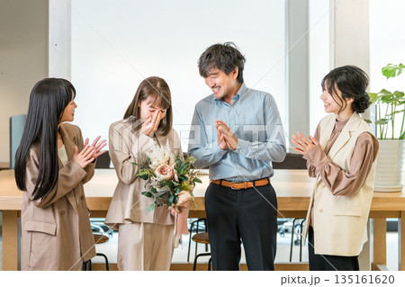 花束を受け取り涙を流すビジネスウーマンと拍手するチームメンバー 花束を受け取り涙を流すビジネスウーマンと拍手するチームメンバー 135161620