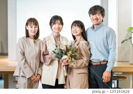 花束を受け取る笑顔のビジネスウーマンと拍手するチームメンバー 花束を受け取る笑顔のビジネスウーマンと拍手するチームメンバー 135161626